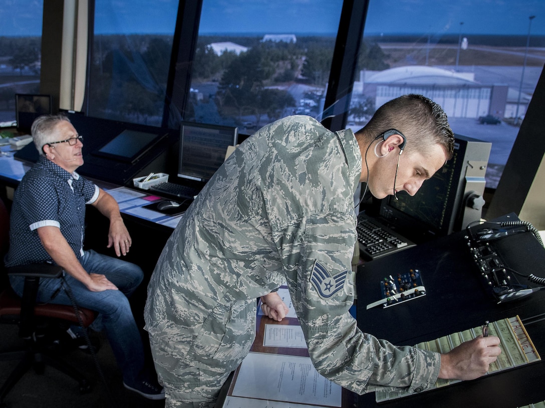Trainer watches airman performing air traffic control duties in tower.