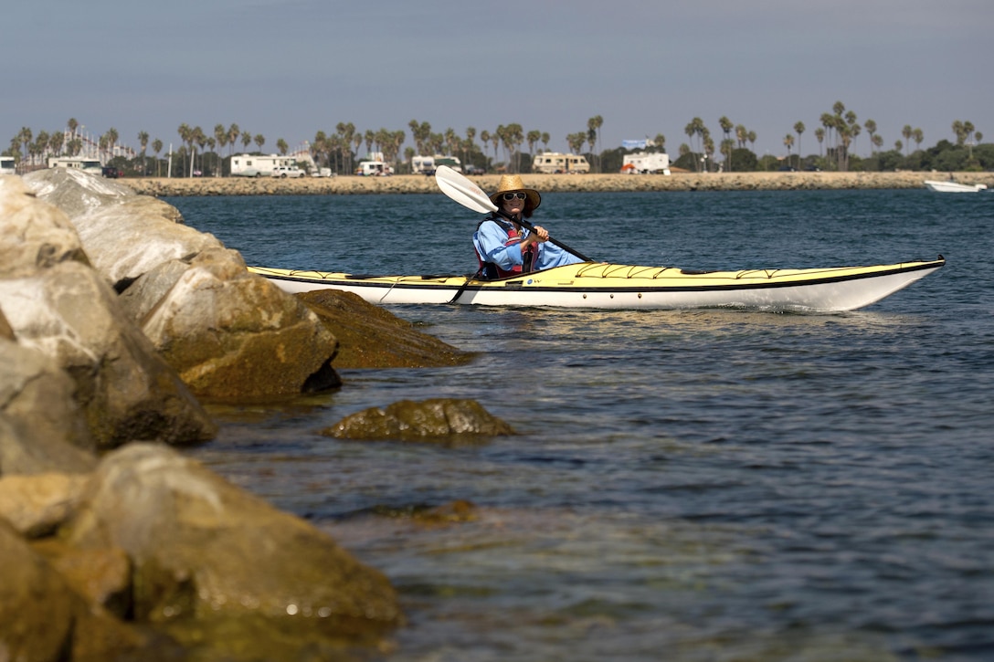 A kayaker paddles near rocks on a bay.