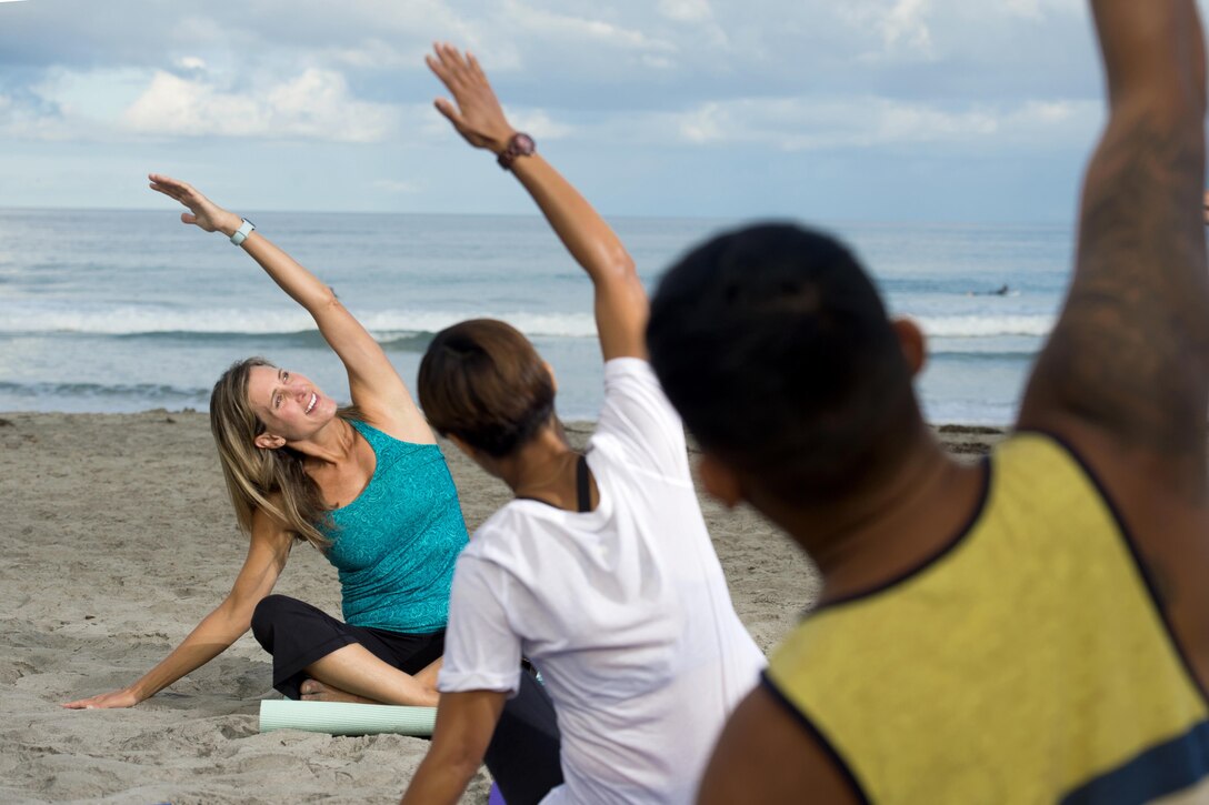 An instructor and two participants raise arms during yoga.