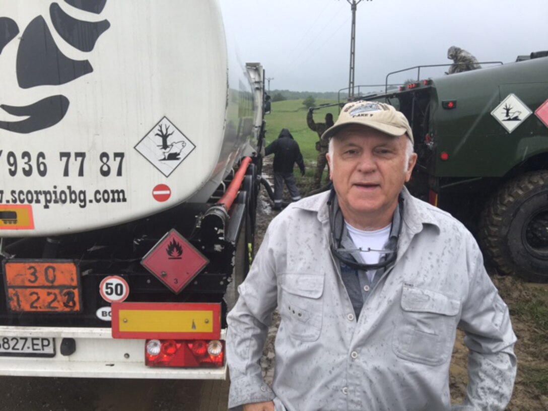 Male civilian facing viewer; fuel truck in background.