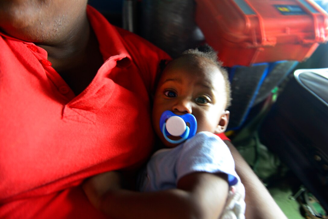 A baby sucking a pacifier in the arms of a caregiver during a helicopter flight.