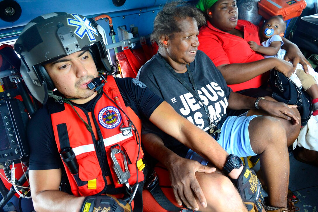 A coast guardsman sits next to two adult and one baby who were rescued from flooded neighborhoods.