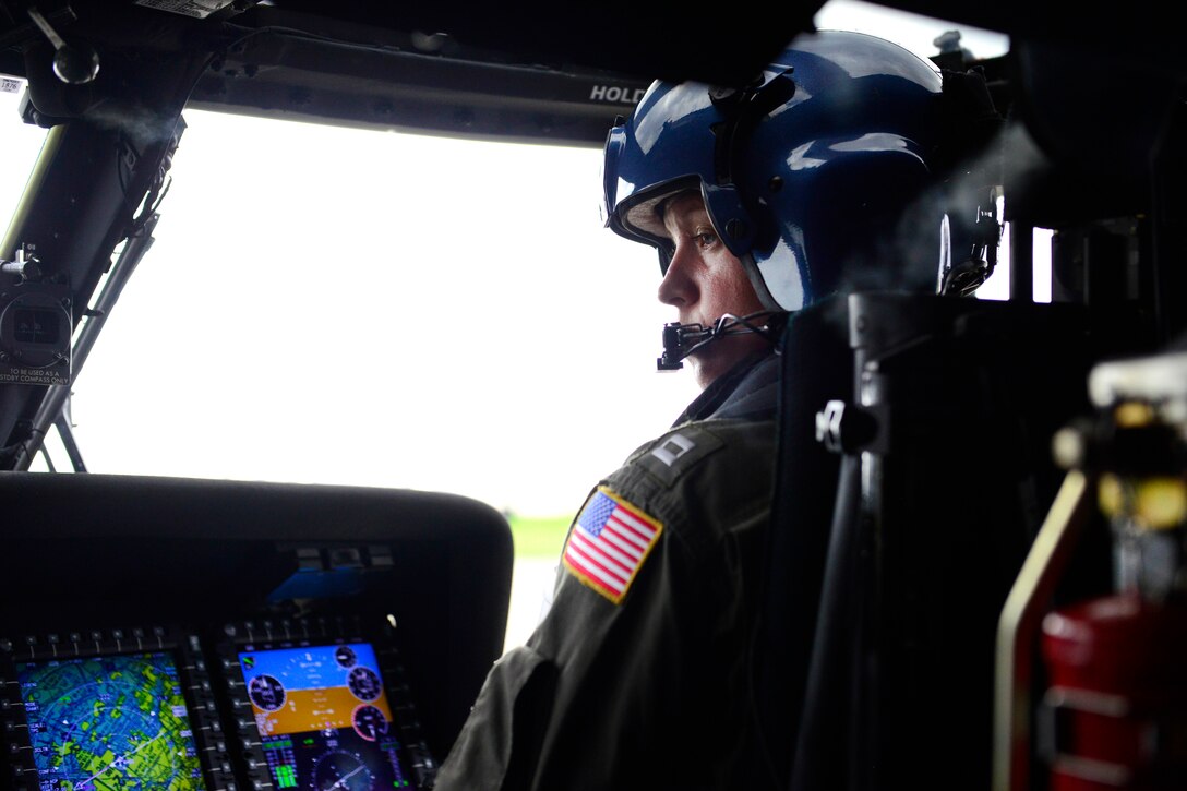 A Coast Guard pilot sits in the cockpit of a helicopter.