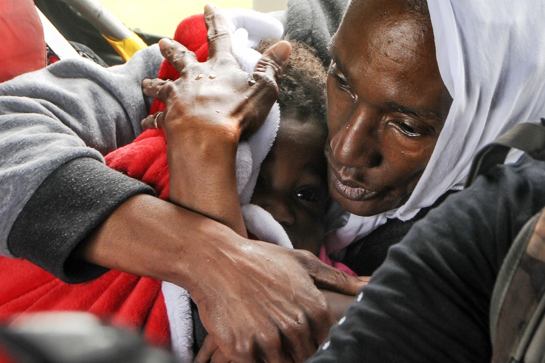 A woman holds a child wrapped in a blanket while in a helicopter.