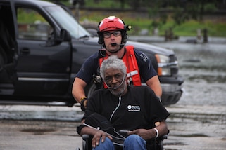 A guardsman pushes an elderly man toward with flooded streets behind them.