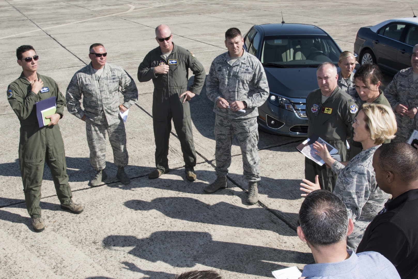 Group of military members in jumpsuits/fatigues conversing on airport pavement.