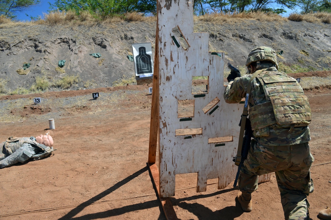 From behind a board, a soldier fires a pistol at a target.