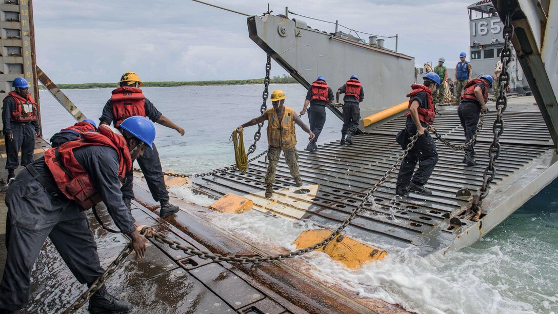 Sailors use chains to connect a landing craft to a ship's well deck.