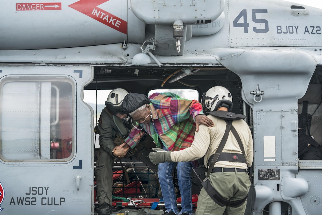 Two sailors help an elderly woman into a helicopter.