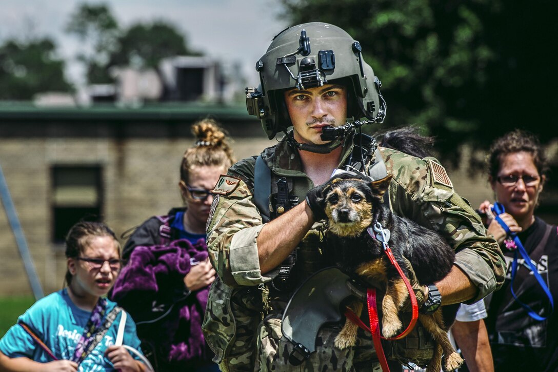 An airman carries a dog and walks in front of family following him.