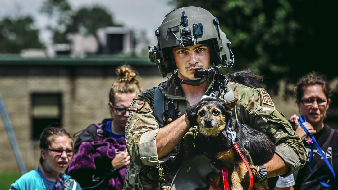 An airman carries a dog and walks in front of family following him.