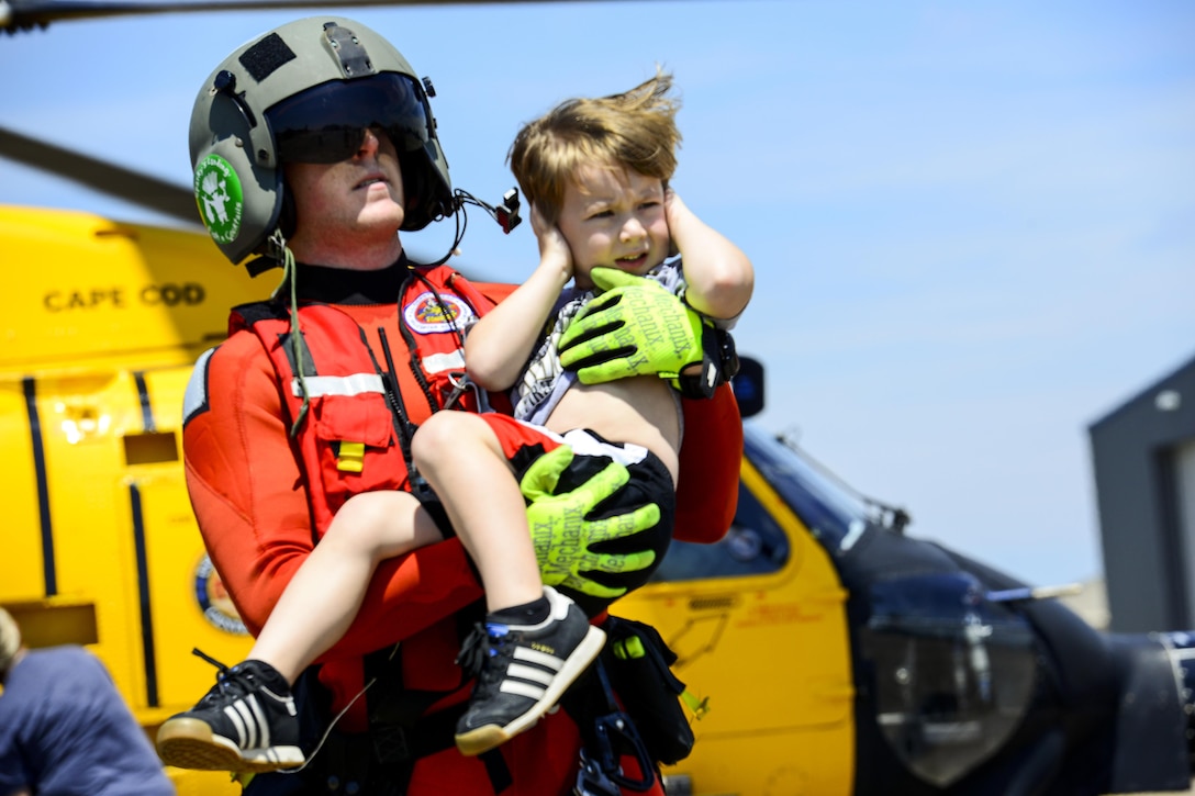 A boy covers his ears as a Coast Guardsman carries him away from a helicopter.