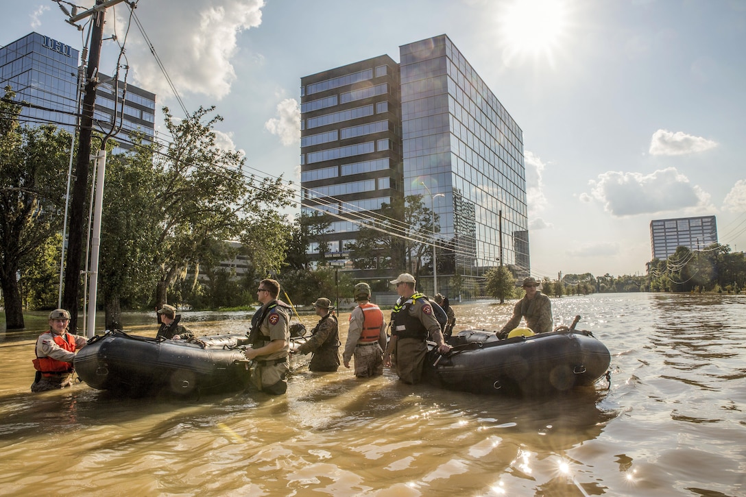 Troops and law enforcement officials pull two inflatable boats through waist-high water in a downtown street.