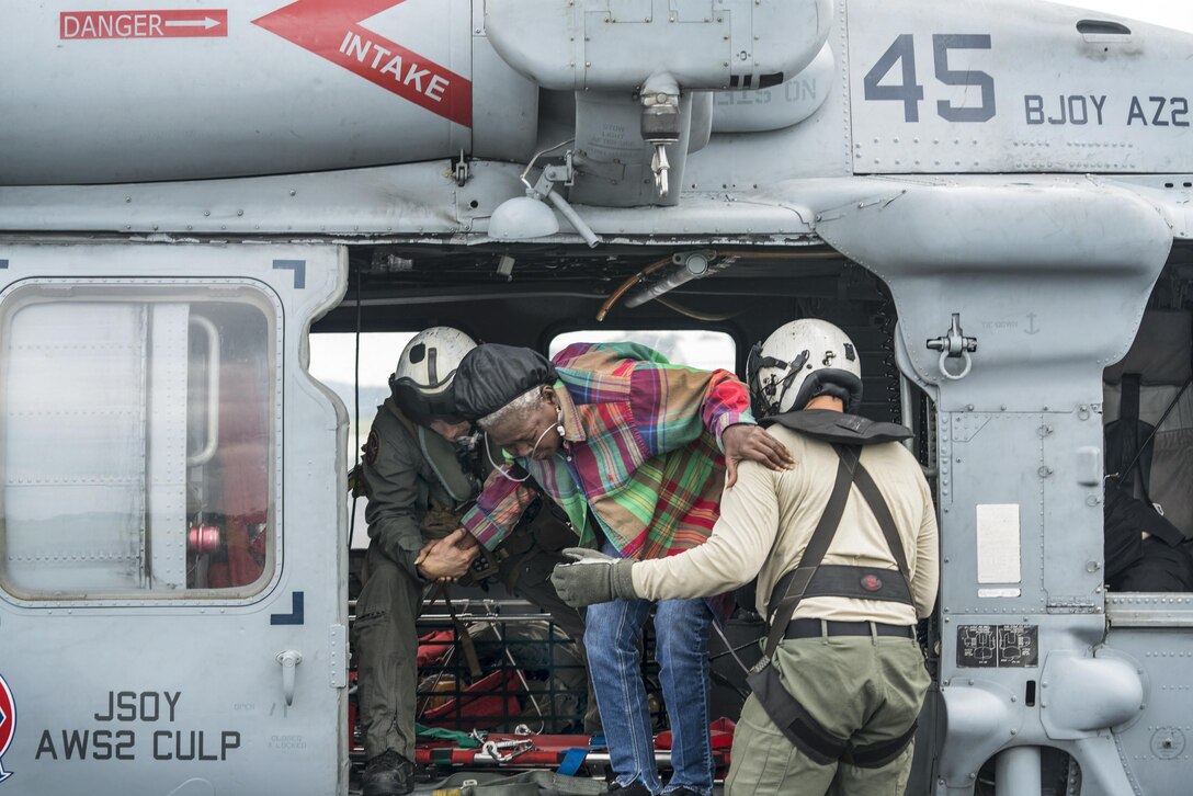 Two sailors help an elderly woman into a helicopter.