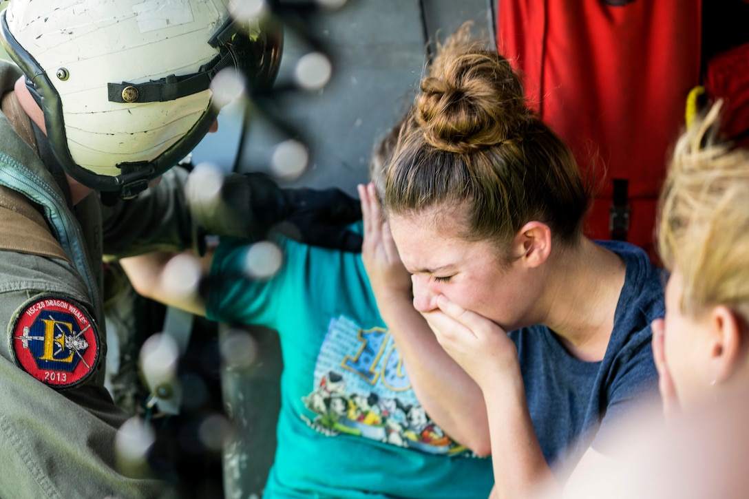 A woman holds her hand over her mouth and cries as a sailor puts his hand on another civilian's shoulder.