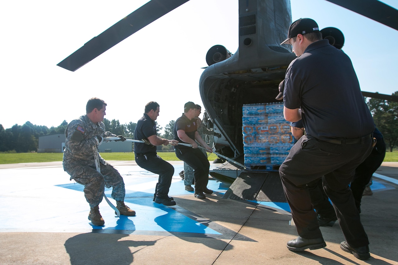 Soldiers unload pallets of water from a helicopter.