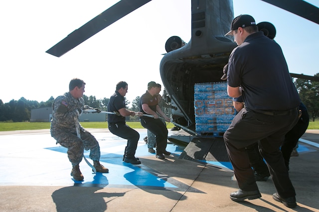 Soldiers work alongside the Liberty Fire Department to unload pallets of water from a CH-47 Chinook helicopter