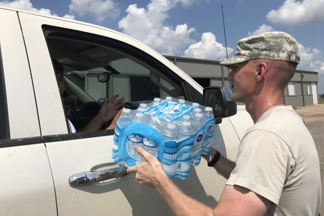 A soldier hands bottled water to a resident sitting in a truck.