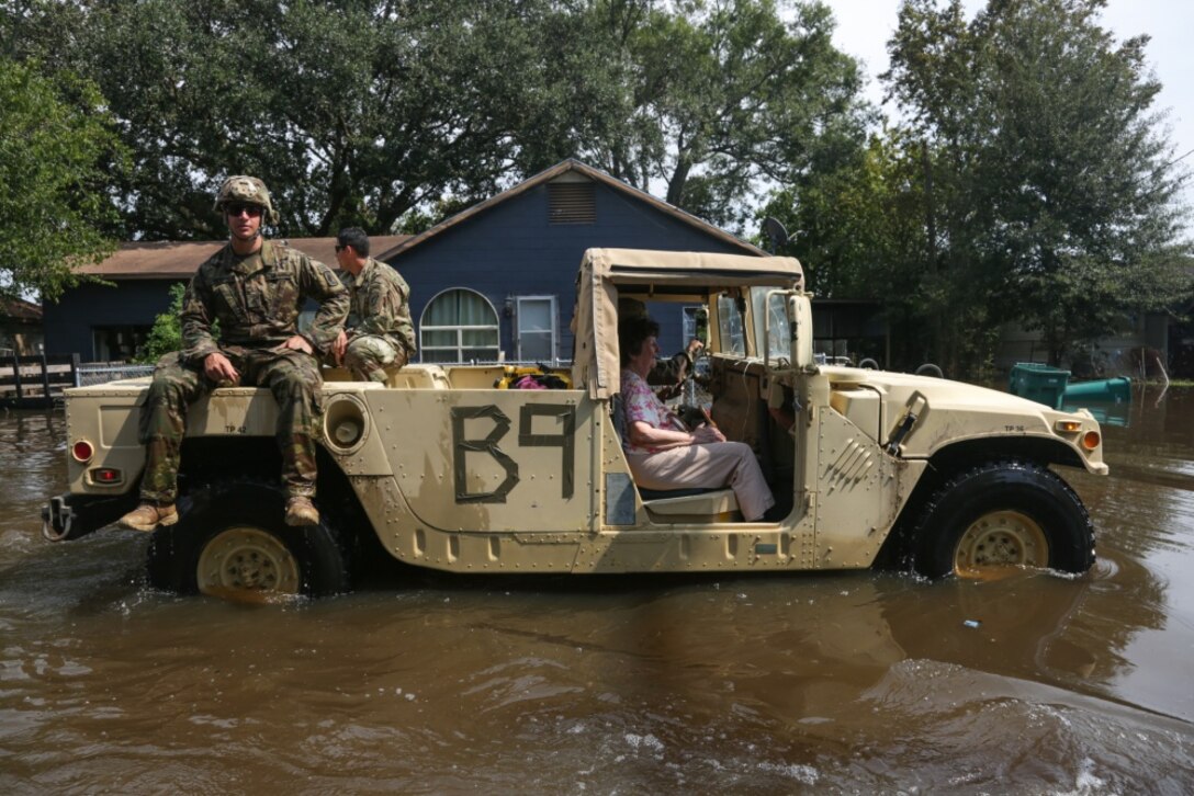 A military vehicle carries a rescued woman and soldiers through flooded streets.