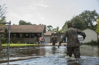 Marine Corps Lance Cpl. Jacob Ramirez (right), an MKR15 Wrecker operator with Detachment Bravo, Marine Wing Support Squadron 473, Marine Air Craft Group 41, 4th Marine Aircraft Wing, Marine Forces Reserve, and Marine Sgt. Ben Tomerlin (center), a platoon sergeant with 14th Marine Regiment, 4th Marine Division, MARFORRES, walk through a flooded street in Orange, Texas, to hand supplies to a woman, Sept. 3, 2017. 14th Marines and Detachment Bravo both based out of Fort Worth, Texas, traveled to Orange to transport supplies to locals affected by Hurricane Harvey which landed in eastern Texas.