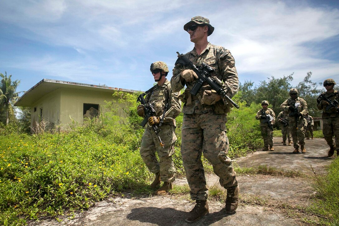 A Marine and a group of soldiers patrol through an area.