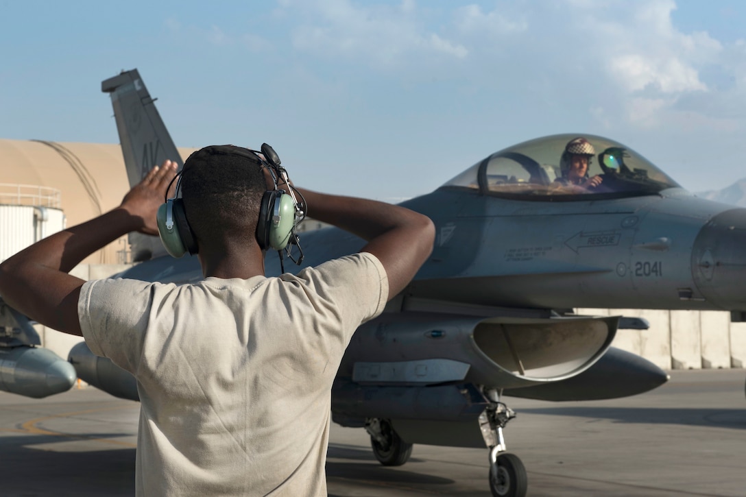 An airman marshals an F-16 Fighting Falcon into a parking spot