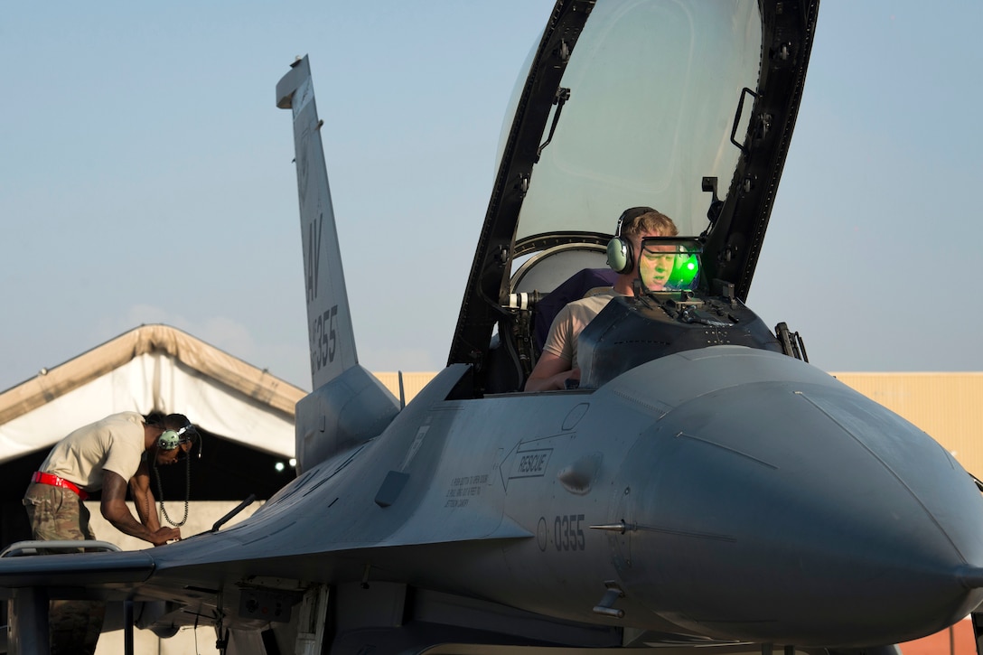 An airman performs final systems checks in the cockpit of an F-16 Fighting Falcon