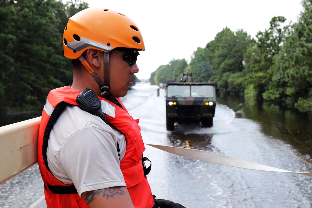 A guardsman looks at a flooded street with a military vehicle in the background.