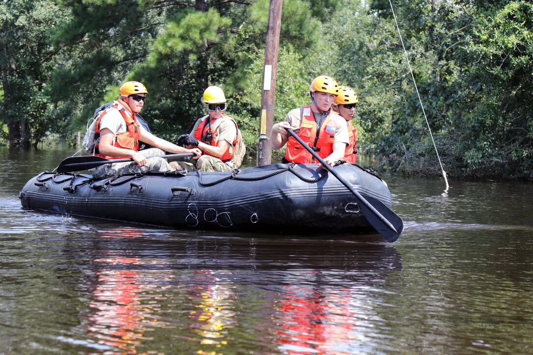 A group of guardsmen paddle a boat through floodwaters.