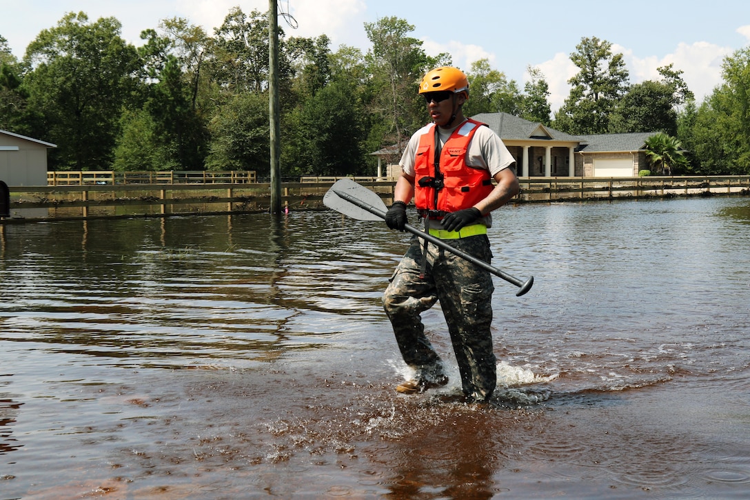 A guardsman walks though floodwaters carrying an oar.