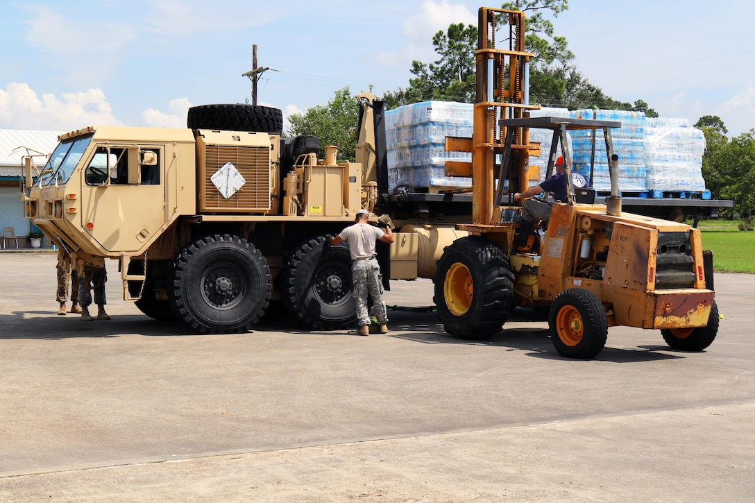 Large vehicles carry pallets of water.