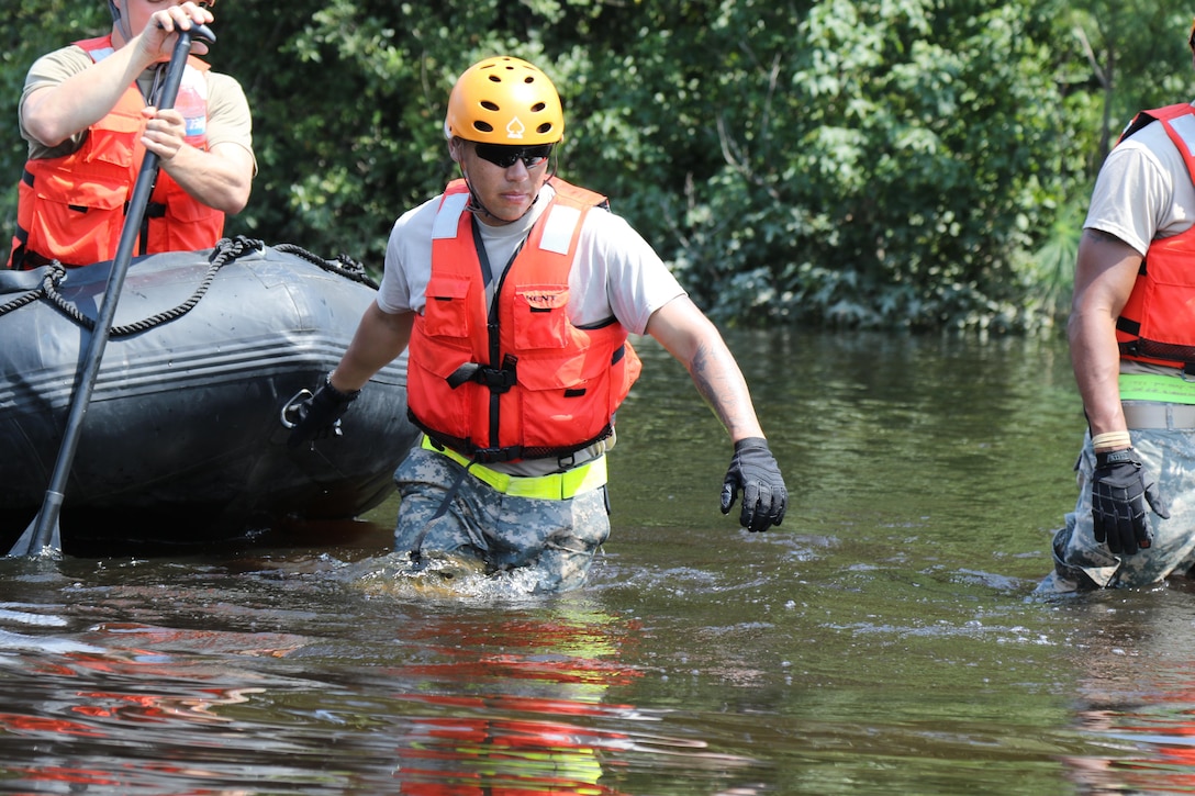 A guardsman pulls a boat though floodwaters.