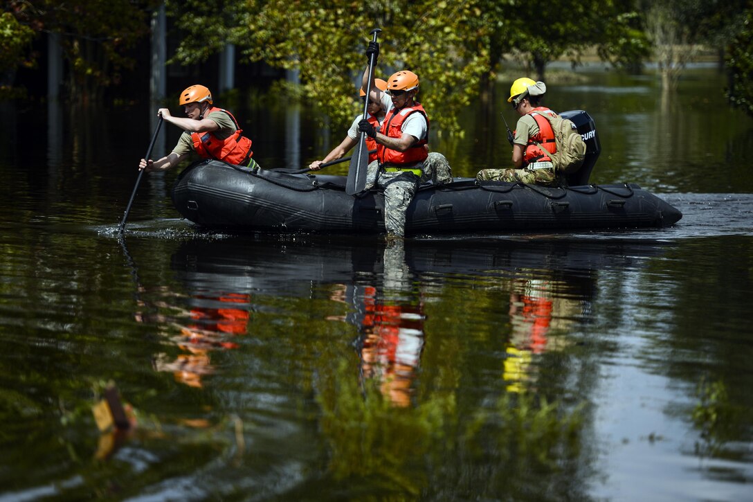 Four soldiers paddle a boat in floodwaters.