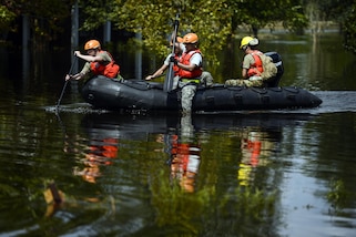 Four soldiers paddle a boat in floodwaters.