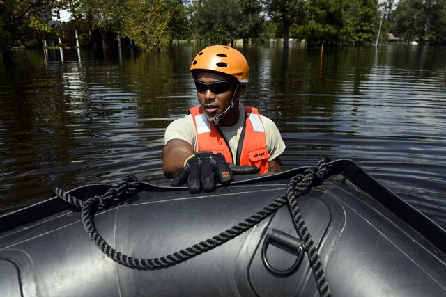 A soldier stands in floodwaters with his hand on a boat.