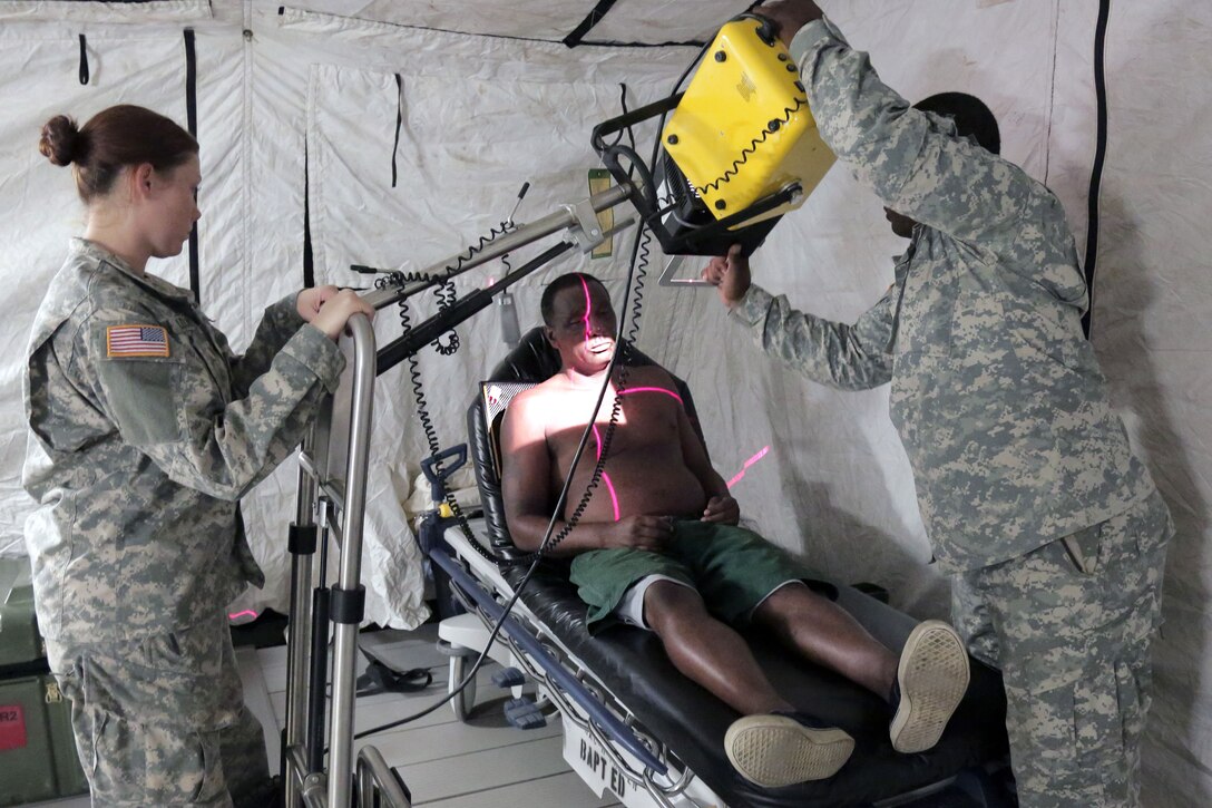 Two soldiers prepare to use an x-ray machine on a person lying down.