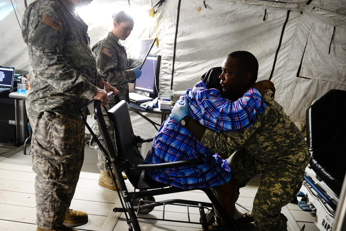 Three soldiers help a women out of a wheel chair.