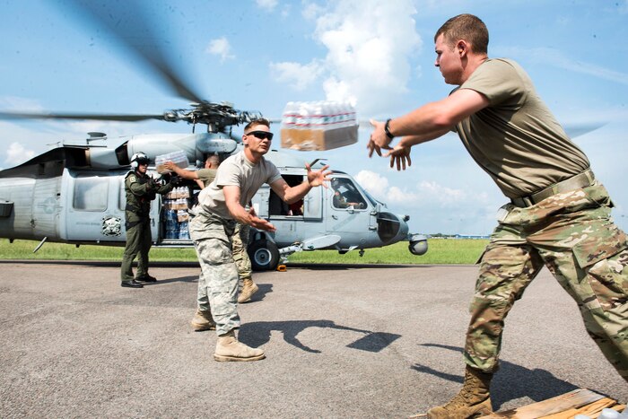 Soldiers and sailors load water onto a helicopter.