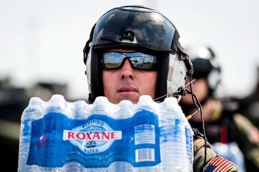 A sailor carries a case of water.