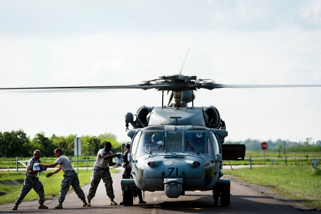 Sailors and soldiers load water and cargo onto a helicopter.