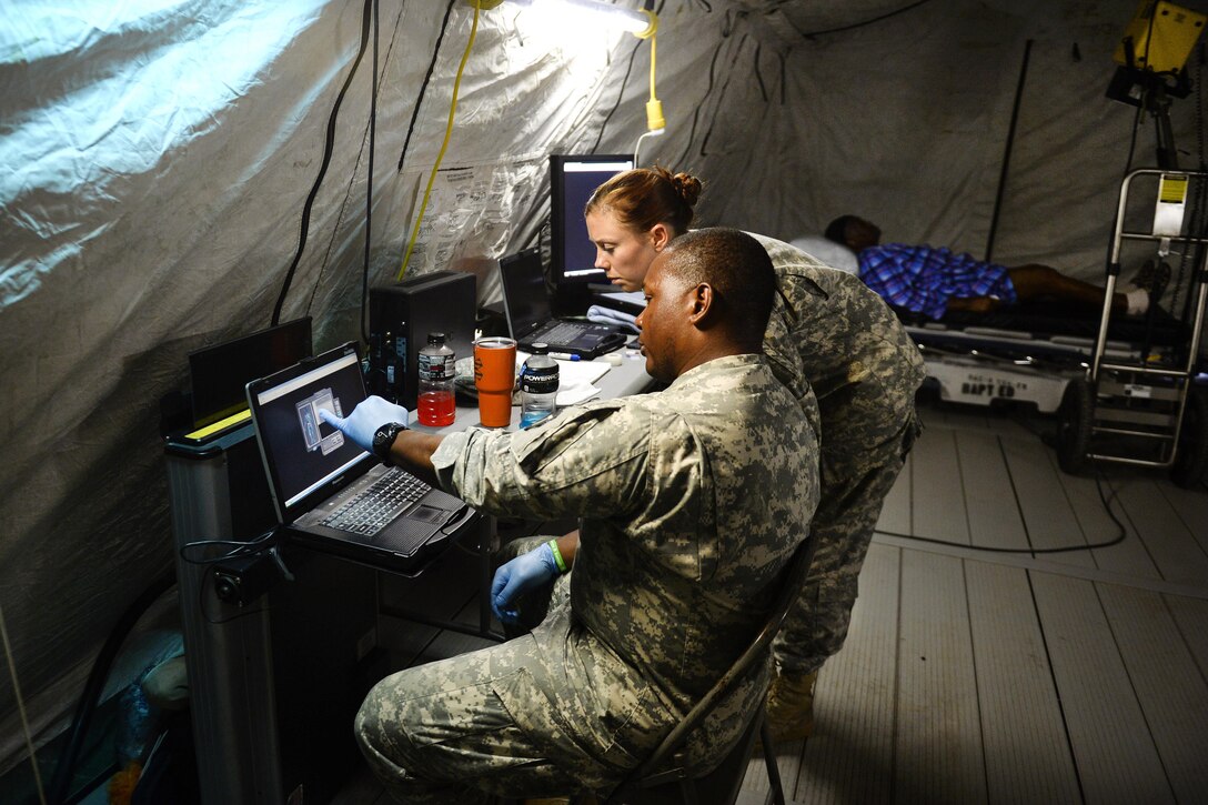 Two soldiers look at a computer screen.