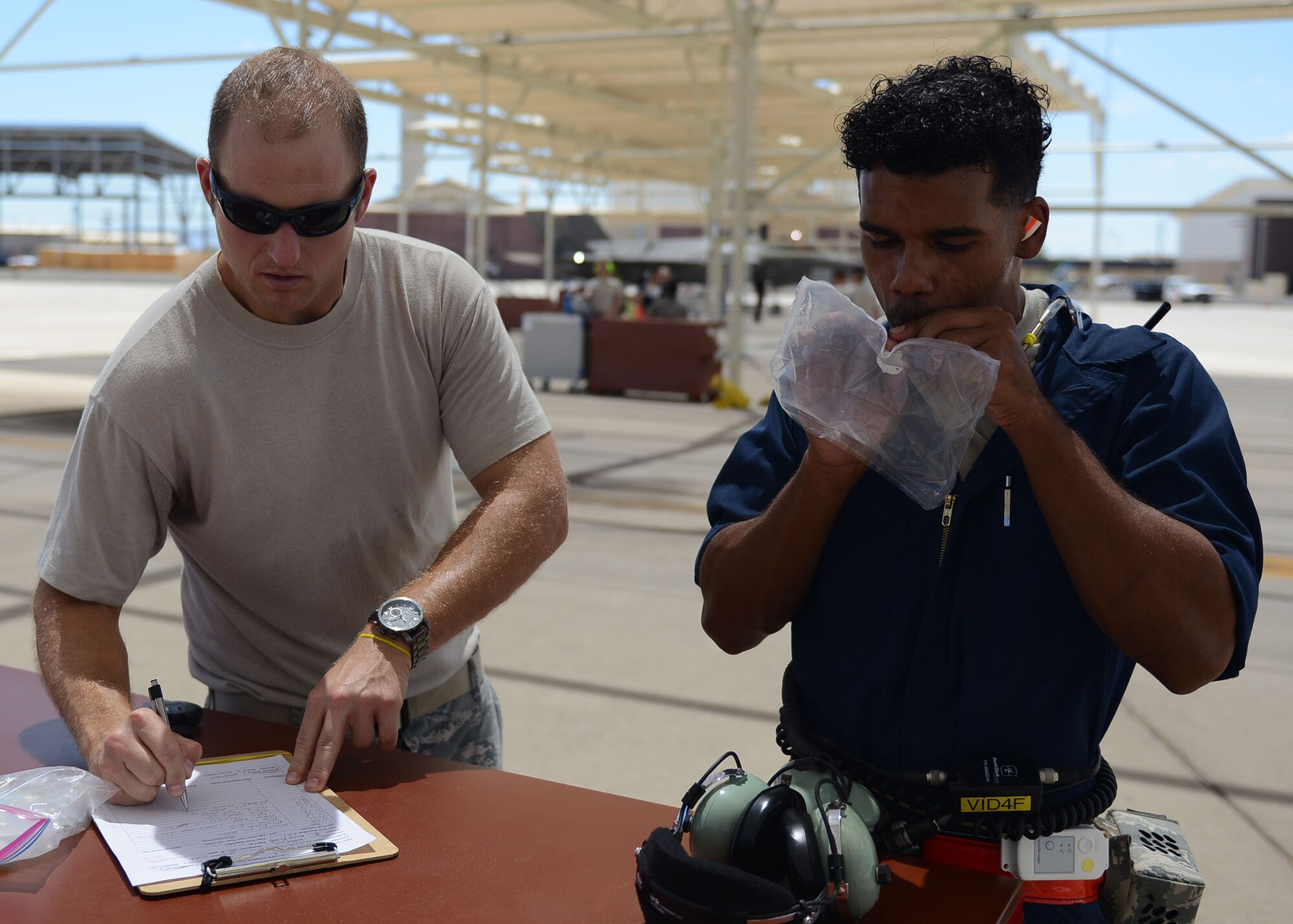 Maj. Jamie Kurzdorfer, School of Aerospace Medicine Force Health Protection branch chief (left), annotates the time when Airman 1st Class Eric Ruiz-Garcia, 63rd Aircraft Maintenance Unit crew chief, gives an air sample at Luke Air Force Base, Ariz., Aug. 22, 2017. Ruiz-Garcia also wore air sampling devices and thermal stress monitors during the launch and recovery of an F-35A Lightning II. The purpose of the test is to collect real time data of the air quality and the core temperatures of the maintainers during a launch. (U.S. Air Force photo/Senior Airman James Hensley)