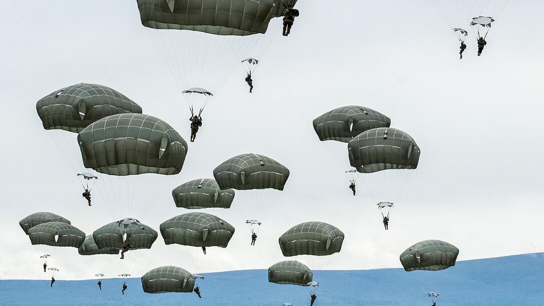 Soldiers with parachutes descend to the ground after jumping from an aircraft.