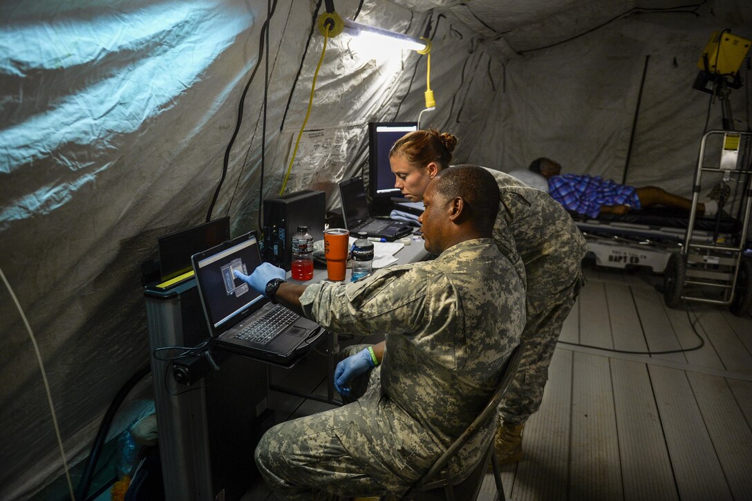 Two soldiers look at an X-ray in a field hospital in a parking lot.