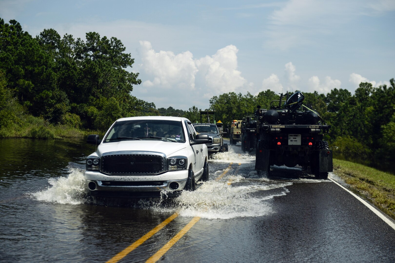 Military vehicles and civilian vehicles drive though a flooded street.