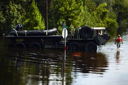 A military vehicle drives through flood waters on a street.