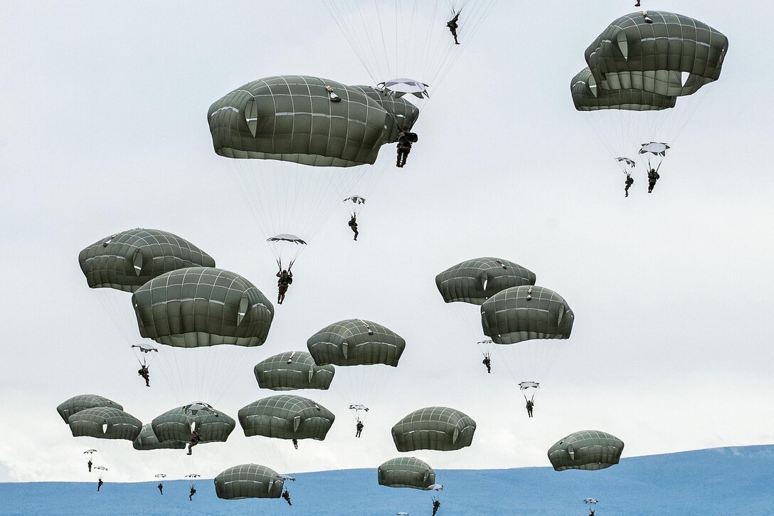 Soldiers with parachutes descend to the ground after jumping from an aircraft.