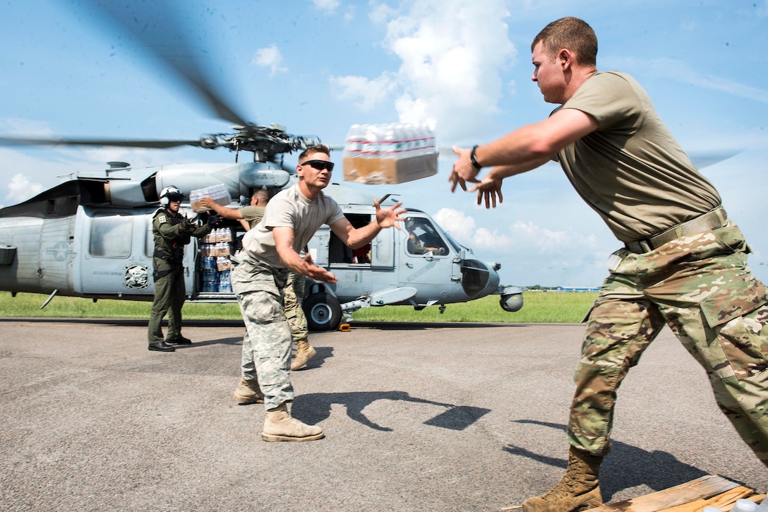 Soldiers and sailors load water onto a helicopter.