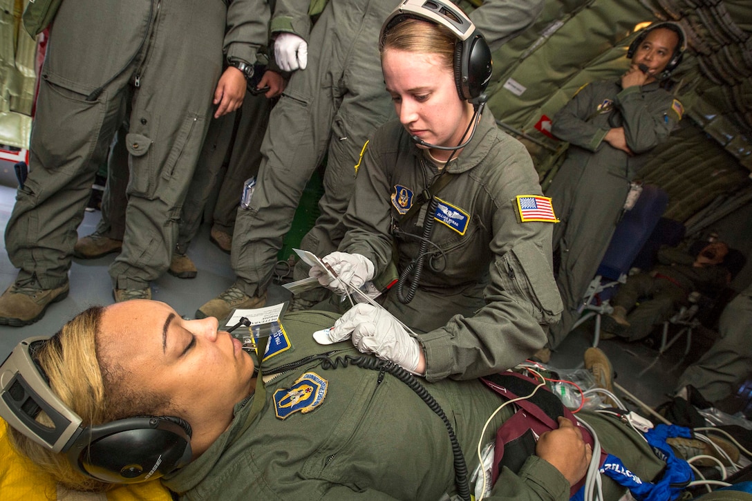 Senior Airman Jacob N. Patterson, kneeling, attaches electrocardiogram electrodes on mock cardiac arrest patient