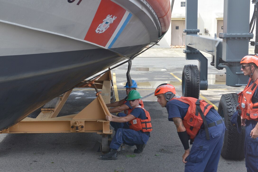 A group of Coast Guard members watch a boat as it is lowered onto a boat cradle.